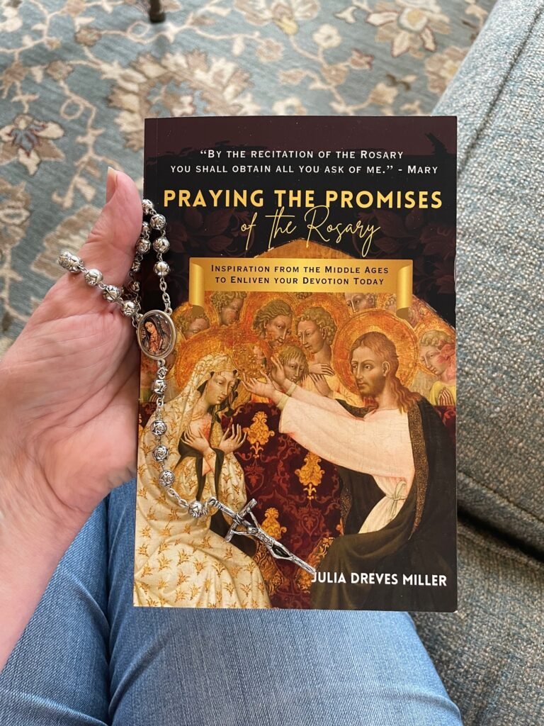 Praying the Promises of the Rosary book on woman's lap, wearing light blue jeans and holding a silver rosary along with the book